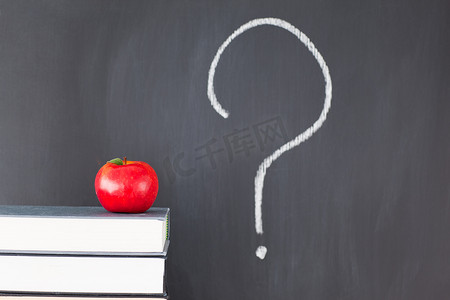 一摞书和孩子摄影照片_一摞书，上面有一个红苹果和一块黑板，上面写着“？”