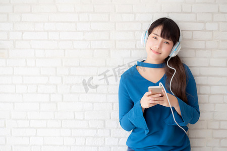 小音响背景摄影照片_美丽的亚洲年轻女子肖像站在水泥混凝土背景上快乐地享受和有趣地听音乐，女孩的生活方式用耳机放松音响收音机，技术概念。