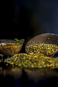 绿豆或月豆在粘土碗中的特写镜头，以及一些水和月豆在黑色光泽表面上充分混合。