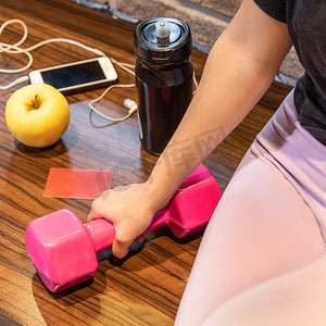 粉色苹果手机摄影照片_手持粉色哑铃、智能手机耳机苹果水瓶的女性