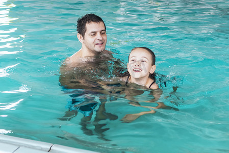 父亲教女孩在游泳池里游泳。