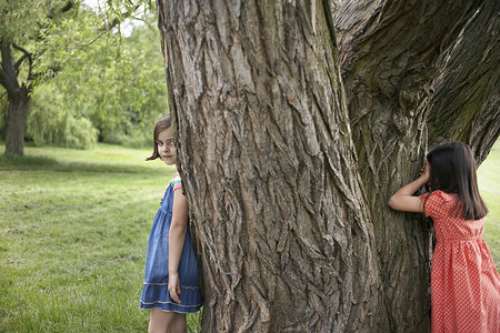 两个女孩在公园的树旁玩捉迷藏