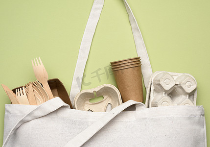 绿色背景中的白色纺织袋和棕色工艺纸制成的一次性餐具