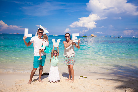 年轻幸福的四口之家在热带度假，带着“爱”这个词