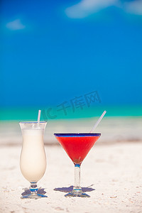 两杯鸡尾酒：白色沙滩上的冰镇果汁朗姆酒和草莓玛格丽塔