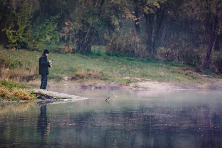 秋日晴天，河湖岸边模糊的渔夫拿着钓竿，水中的倒影