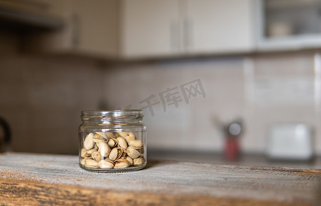 桌子上的罐子摄影照片_开心果放在一个罐子里，站在一张白色的老式桌子上，背景是厨房。