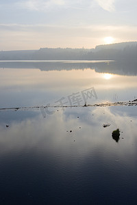 我是插座摄影照片_垂直朦胧的日落反映在水库边缘平静的水中