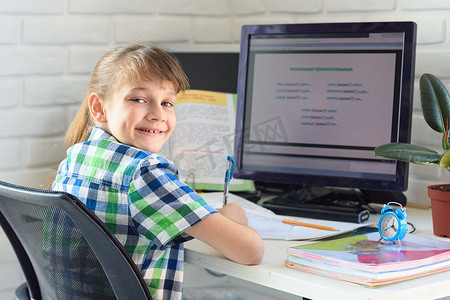 课程框架摄影照片_一个满意的孩子坐在电脑桌旁，看着框架