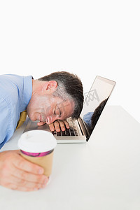 疲惫的男人拿着咖啡睡在笔记本电脑上