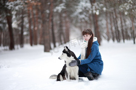 哈士奇哈士奇摄影照片_冬天森林里，女孩和西伯利亚哈士奇狗坐在雪地里