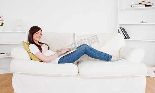 躺沙发摄影照片_迷人的红发女性躺着时用笔记本电脑放松