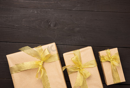 用牛皮纸包裹的盒子，用金色丝带绑着蝴蝶结，木制背景上的礼物