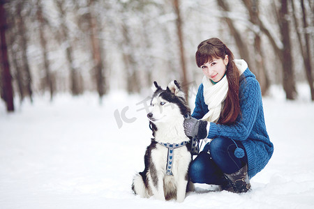 冬天森林里，女孩和西伯利亚哈士奇狗坐在雪地里