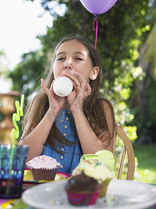气球吹气摄影照片_小女孩在户外生日聚会上吹气球