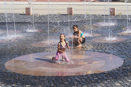 在阳光明媚温暖的日子里，孩子们在外面的喷泉里玩耍。