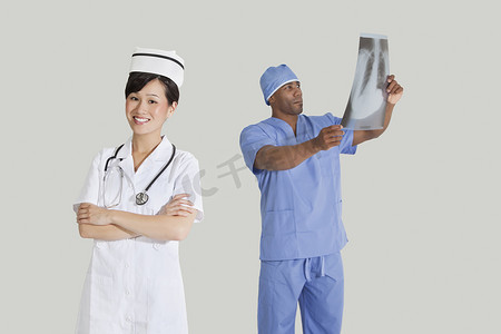 快乐的年轻护士与男外科医生在灰色背景下检查 X 射线报告的肖像
