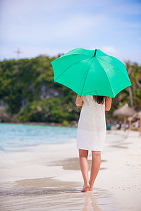 白色海滩上有绿色伞的年轻女孩