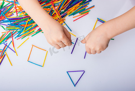 孩子们在白色背景上用彩色棍子制作几何形状