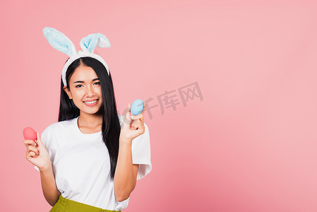 耳钉摄影照片_戴着兔耳微笑的女人手上拿着彩色复活节彩蛋礼物