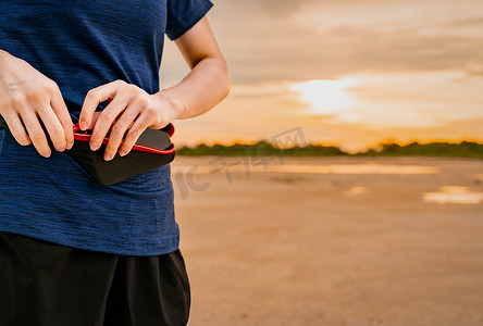 年轻的亚洲女跑步者跑步前将智能手机放在腰包里