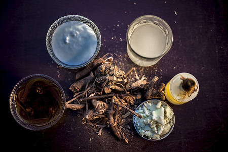 原始的阿育吠陀草药 Chitrak/Plumbago zeylanica 根位于棕色闪亮的表面上，带有一些酪乳、酥油或澄清黄油、其提取物、凝乳和蜂蜜，用于阿育吠陀疗法。