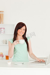 华丽的红发女性在厨房里用笔记本电脑放松