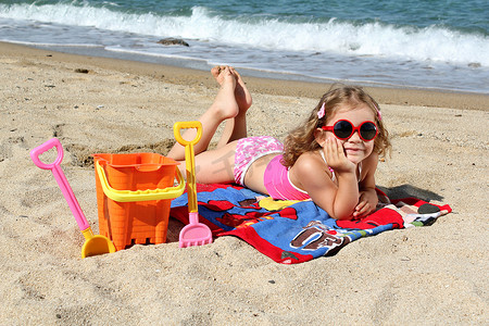 戴着墨镜躺在沙滩上的小女孩
