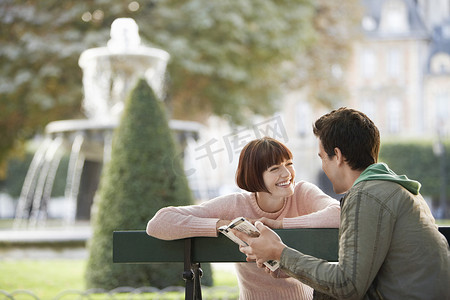快乐的年轻夫妇在城市公园长凳上阅读指南书
