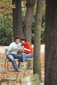 年轻夫妇在树干旁的公园椅子上阅读指南