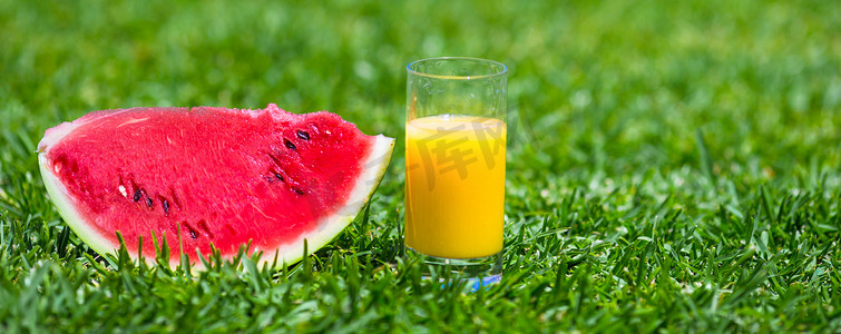 夏季和新鲜主题：绿草上红熟片西瓜和一杯橙汁