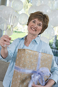 鸡年元宝福袋摄影照片_一位快乐的高级女性在母鸡聚会上拿着礼物和香槟笛的肖像