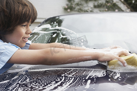 一个小男孩用海绵洗车的特写侧视图