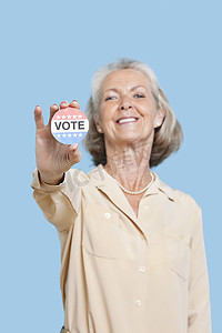 高级英语摄影照片_蓝色背景下持有选举徽章的高级女性肖像