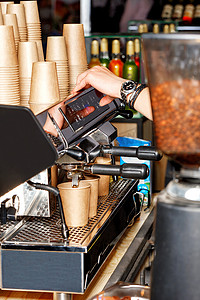 空包纸杯摄影照片_咖啡师在咖啡机和一张空纸杯幻灯片的背景下准备咖啡并将其倒入纸杯中。