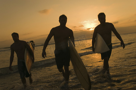 日落时三名冲浪者携带冲浪板出海冲浪的全长