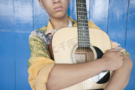 一个十几岁男孩的中间部分，吉他靠在木镶板上
