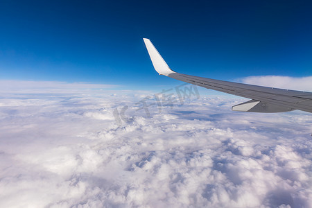 飞机高空摄影照片_从乘客窗口可以看到蓝天下的飞机机翼在高空云层之上飞行。