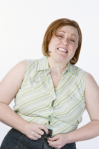 肥胖女性摄影照片_白色背景中无法扣上牛仔裤的恼怒肥胖女性的肖像