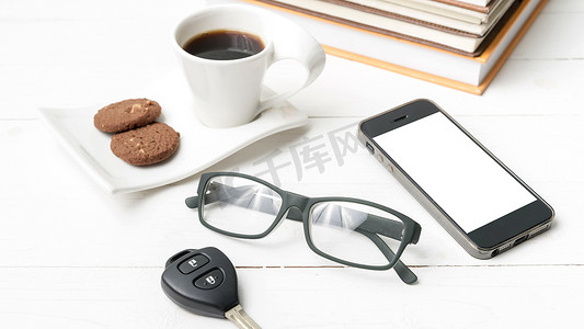 带饼干、电话、车钥匙、眼镜和一摞书的咖啡杯