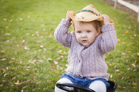 戴着牛仔帽、在外面玩玩具拖拉机的幼儿