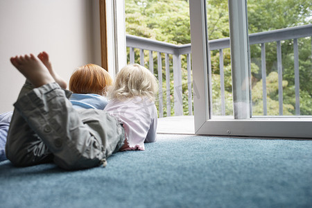 家里的门摄影照片_年轻的姐妹们躺在家里的地毯上，透过阳台向外望去