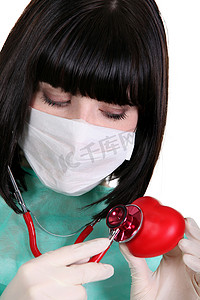 蓝绿色摄影照片_带手术面罩的黑发护士用听诊器在红心上