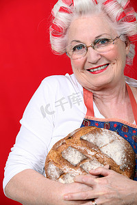 头发上有卷发的老年妇女拿着新鲜出炉的面包