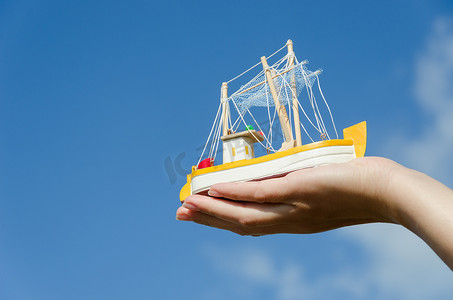 模型船摄影照片_蓝天背景棕榈上的木船玩具