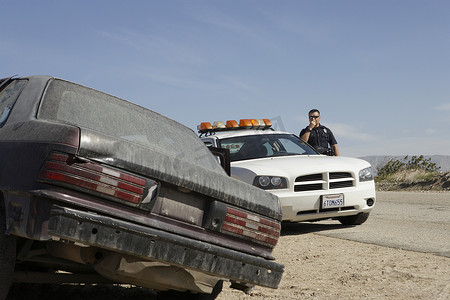 警察在沙漠公路上的废弃汽车附近使用CB无线电