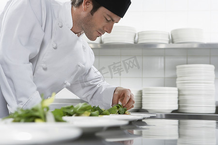 一位男厨师在厨房准备沙拉的侧视图