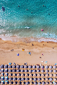 夏季日落时，沙滩鸟瞰图，五颜六色的遮阳伞，人们在海湾里游泳，海水透明。