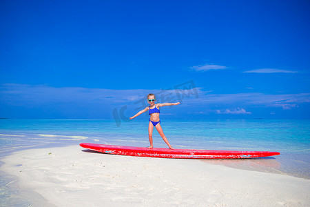 小女孩在热带海滩的冲浪板上玩得开心