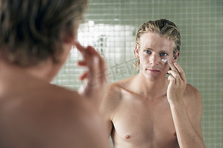 英俊的年轻人在镜子前涂抹面霜